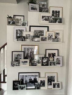 a wall filled with pictures and frames on top of a stair case next to a banister