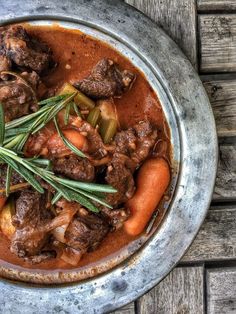 a bowl filled with stew and vegetables on top of a wooden table