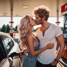 a man and woman kissing in front of a car at a gas station while holding each other's hands