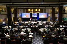 a large group of people sitting at tables in front of big screens on the wall