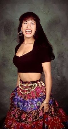 a woman in a black top and colorful skirt with her eyes closed, smiling at the camera