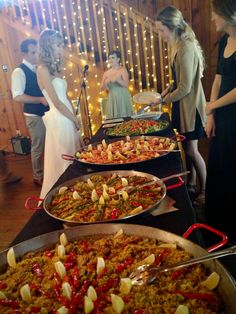 a buffet table with many plates of food on it and people in the background standing around