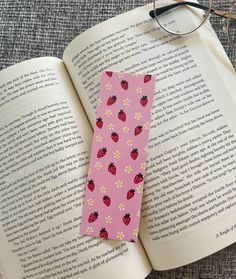 a pink bookmark with ladybugs and daisies on it next to an open book