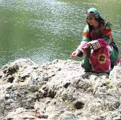 a woman sitting on top of a rock next to a body of water