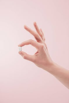 a woman's hand holding a pill in front of a pink background