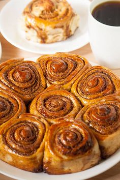 cinnamon rolls on a white plate next to a cup of coffee