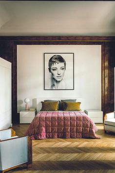 a bedroom with a bed, chair and painting hanging on the wall above it's headboard