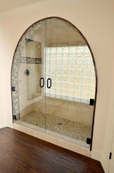 an arched glass shower door in a bathroom with wood flooring and white walls on the wall