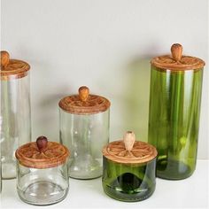 four glass jars with wooden lids on a white counter top next to each other and an acorn in the middle