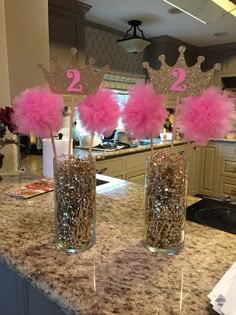 two vases filled with pink feathers on top of a marble countertop in a kitchen