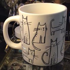 a white coffee cup with cats on it sitting on a glass table next to some glasses