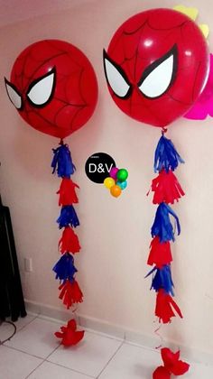 two balloons with spiderman faces and tassels hanging from the ceiling in front of a wall