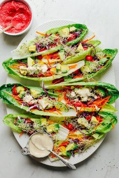 four lettuce wraps on a plate with dressing next to it and a bowl of sauce