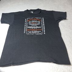 a black t - shirt with an orange and white label on the front that says milwaukee