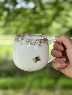 a hand holding a coffee cup with a bee painted on it