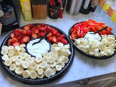 two plates filled with bananas, strawberries and other fruit on top of a counter