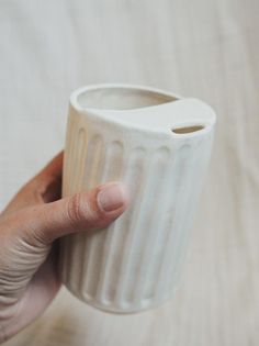 a hand holding a white ceramic cup on top of a table