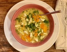 a bowl of chicken noodle soup with carrots and parsley