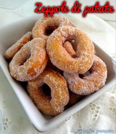 a white bowl filled with sugar covered donuts on top of a lace tablecloth