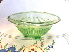 a green glass bowl sitting on top of a white table cloth with flowers in it