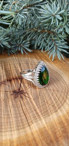 a green ring sitting on top of a piece of wood next to a pine tree