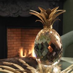 a glass table with a gold pineapple on it and a fire place in the background