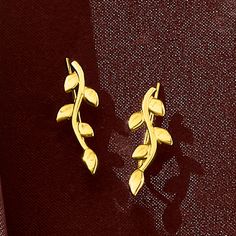 two gold earrings sitting on top of a red cloth