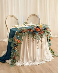 the table is decorated with blue and orange flowers, greenery and gold candlesticks