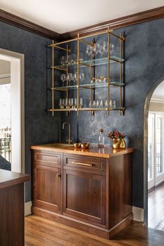 a bar with wine glasses on it in the middle of a room that has blue walls and wood flooring