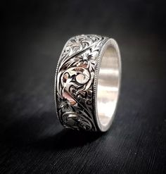 a silver ring with intricate designs on the inside and outside, sitting on a black surface