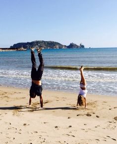 two people are doing handstands on the beach