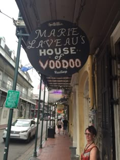 a woman standing under a sign on the side of a building next to a sidewalk