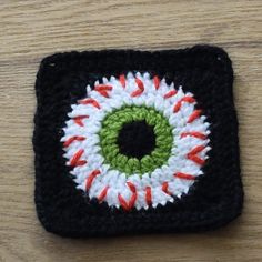 a crocheted square with an eye in the center on a wooden table top