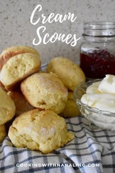 cream scones are piled on top of each other with butter and jam in the background