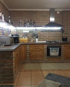 a kitchen with brick walls and tile flooring is shown in this image, there are lights on above the stove