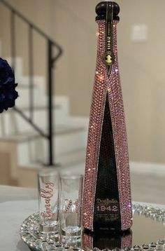 a bottle with pink crystals on it sitting on top of a table next to glasses