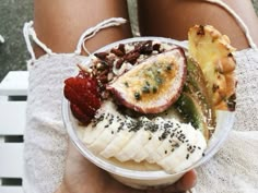 a person holding a bowl with fruit and nuts in it while sitting on a towel