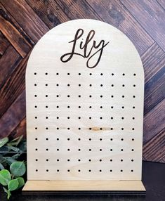 a wooden sign with the word lily written in black ink on it next to a plant