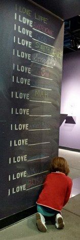 a little boy sitting on the ground in front of a wall with writing on it