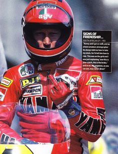 a man in a red racing suit and helmet holding his hand up to the camera