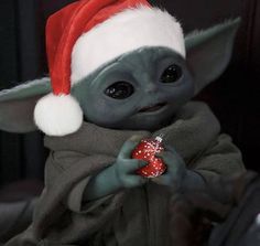 a baby yoda doll wearing a santa hat and holding a candy ornament