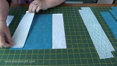 a person cutting up strips of fabric on a piece of green paper that is being sewn together