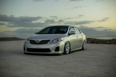 a silver car parked on top of a dirt road next to the ocean and clouds