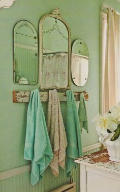 a bathroom with green walls and two mirrors on the wall, flowers in a vase next to it