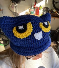 a woman wearing a blue crocheted hat with yellow and black eyes on it