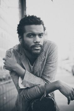 a black and white photo of a man leaning against a wall with his arms crossed