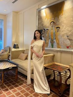 a woman standing in a living room next to a couch and coffee table with a painting on the wall behind her