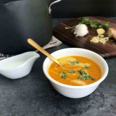 a white bowl filled with soup next to a cutting board and pot on a table