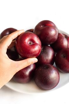 a white plate topped with lots of plums next to a person's hand