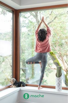 a woman doing yoga in front of a window with her dog sitting on the windowsill